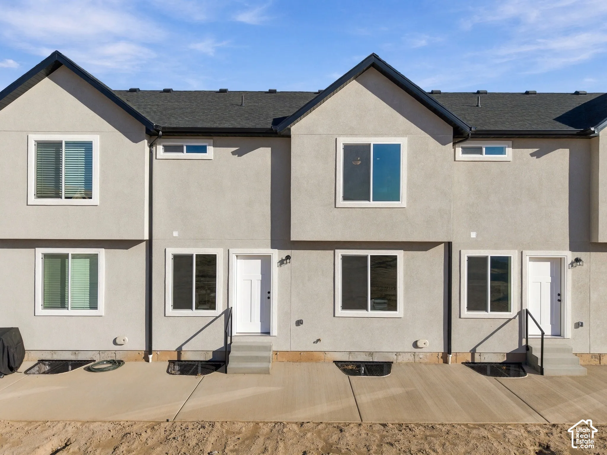 Stucco exterior with multiple windows, individual white entry doors, and a concrete patio