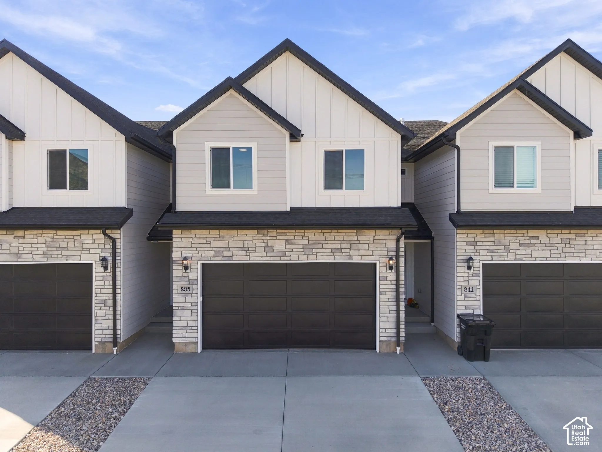 Contemporary exterior featuring stone accents, dark garage doors, and a concrete driveway