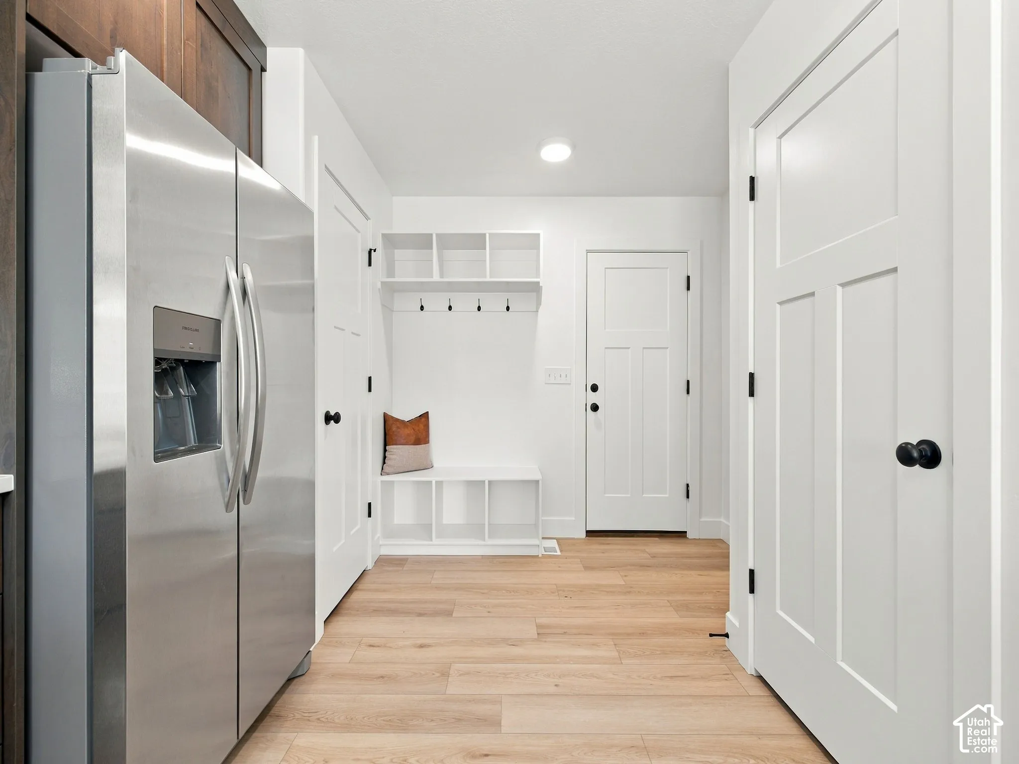 Stainless steel refrigerator, built-in shelving, coat hooks, wood-finish flooring, and white panel doors