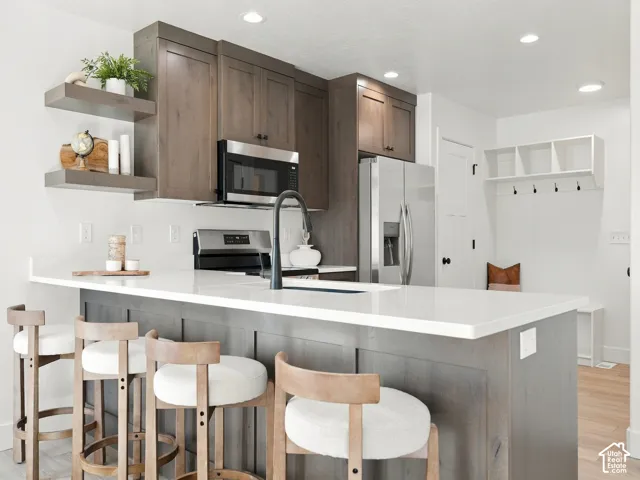 Kitchen featuring a large island with white countertops, dark wood cabinetry, stainless steel appliances, and integrated recessed lighting