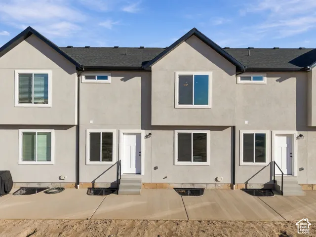Stucco exterior with multiple windows, individual white entry doors, and a concrete patio
