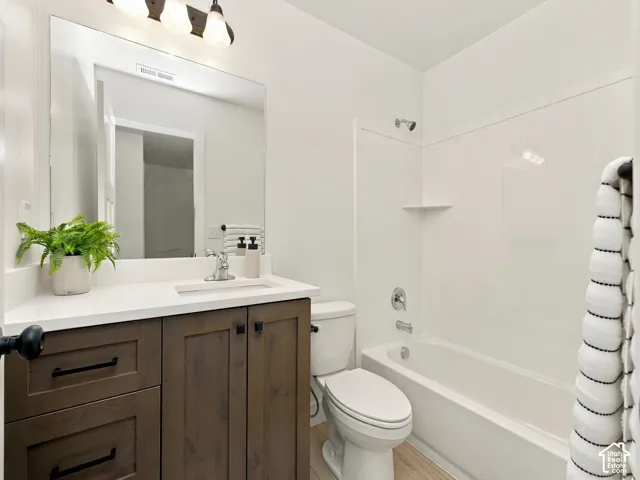Bathroom featuring a wood-finish vanity with dark hardware, a white countertop with an integrated sink, a rectangular mirror, a three-light fixture, and a bathtub with a shower
