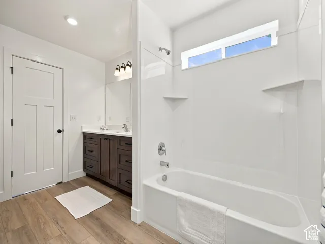 White paneled door, wood-finish flooring, dark wood-finish dual vanity with white countertop, chrome fixtures, and a white tub with integrated shelving