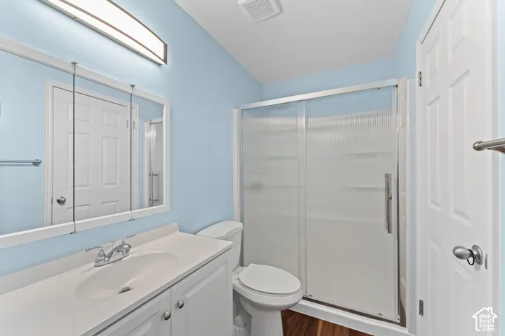 Vanity with integrated sink, tri-fold medicine cabinet, sliding glass shower enclosure, wood-finish flooring, and white paneled door