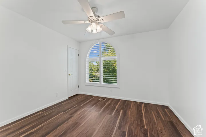 Arched window with louvered shutters, wood-finish flooring, ceiling fan with integrated lighting, and a paneled door