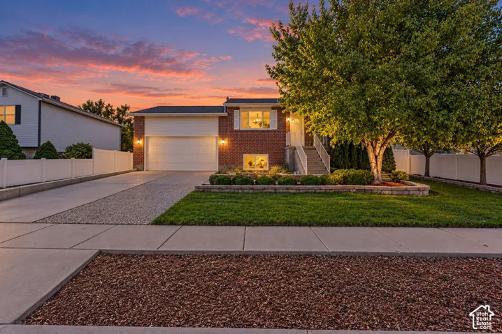 Brick facade residence featuring an attached garage, concrete driveway with gravel accents, and mature front yard landscaping