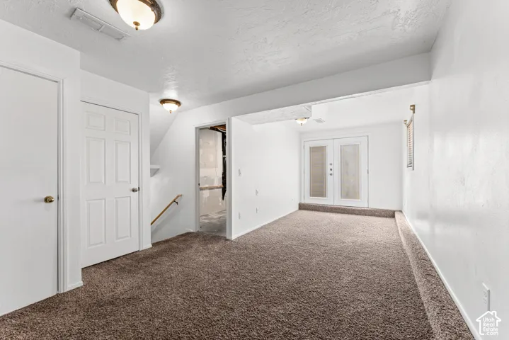 Carpeted room with white walls, ceiling-mounted lighting, and a double-door entry