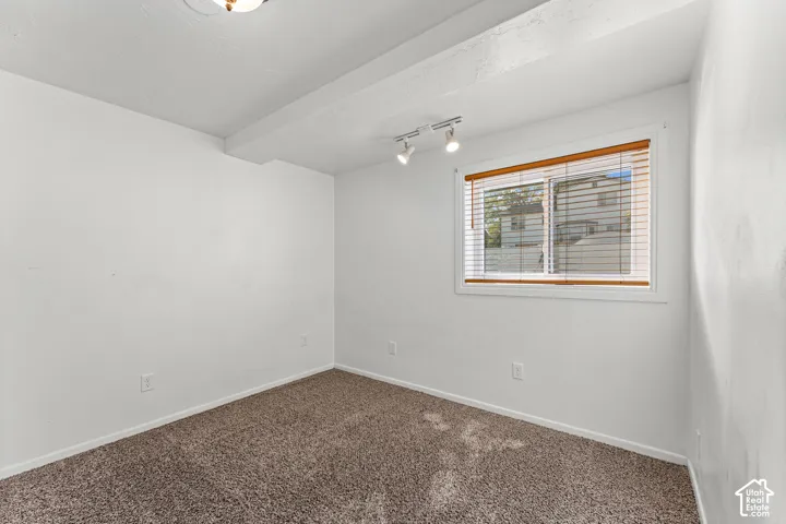 Recessed ceiling beam, track lighting, neutral carpeting, window with blinds, and a flush mount ceiling light fixture