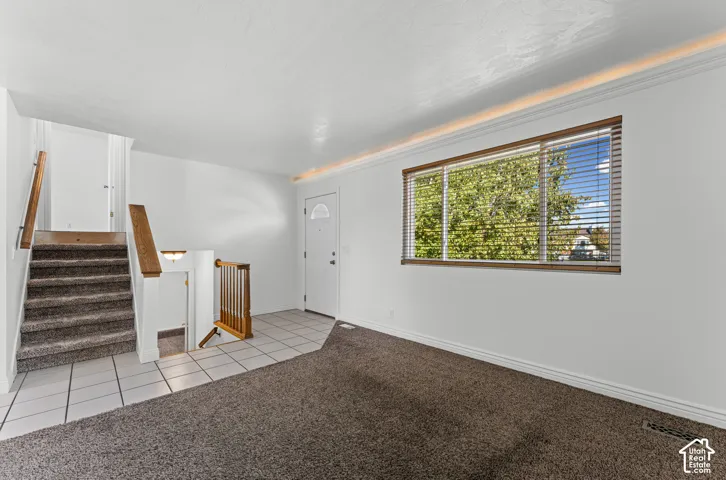 White entryway door with frosted glass insert, neutral tile flooring, and carpeted stairs with wood handrails