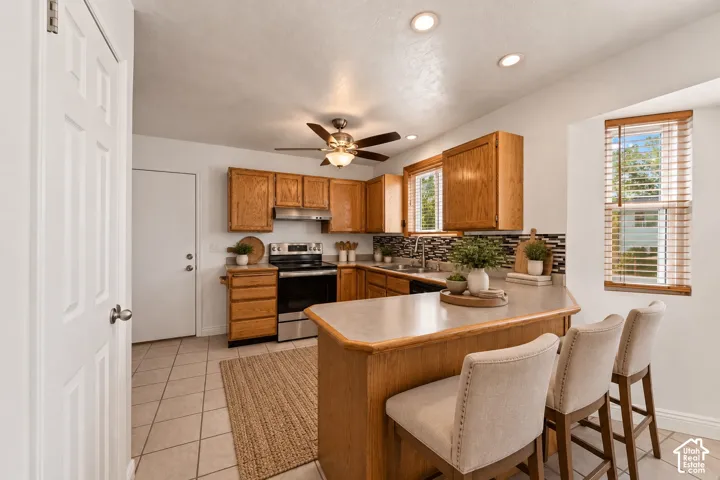 Kitchen featuring wood cabinetry, stainless steel appliances, tile flooring, recessed lighting, and a multi-level island with seating