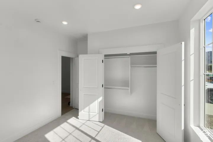 Recessed lighting, light-toned carpeting, white walls, and a built-in closet with double bifold doors
