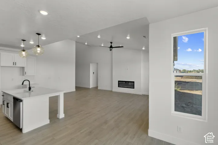 Open-concept interior featuring wood-finish flooring, recessed lighting, a built-in electric fireplace, and a kitchen island with a sink and pendant lighting