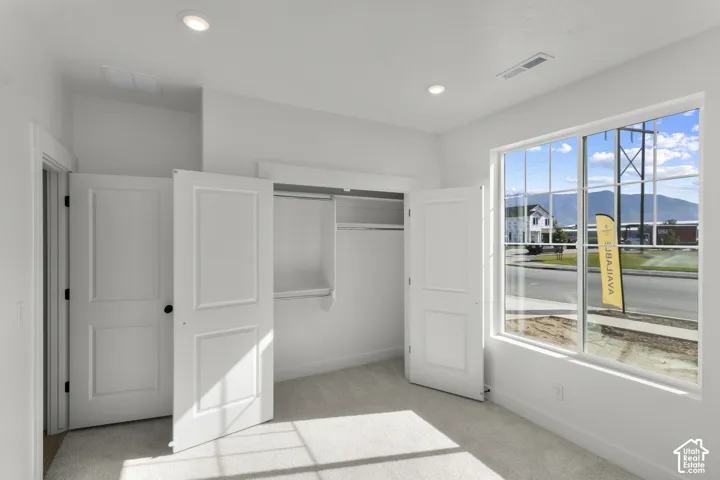 Recessed ceiling lighting, large window with grid pattern, carpeted flooring, built-in closet with shelving and hanging rod, paneled interior doors