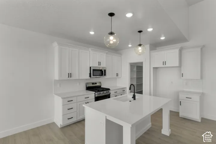 White shaker cabinetry with black hardware, recessed lighting, wood-finish flooring, and a central island with an integrated sink