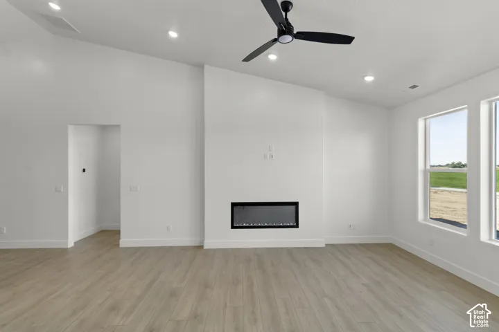 Vaulted ceiling with recessed lighting, linear electric fireplace, wood-finish flooring, and multiple windows