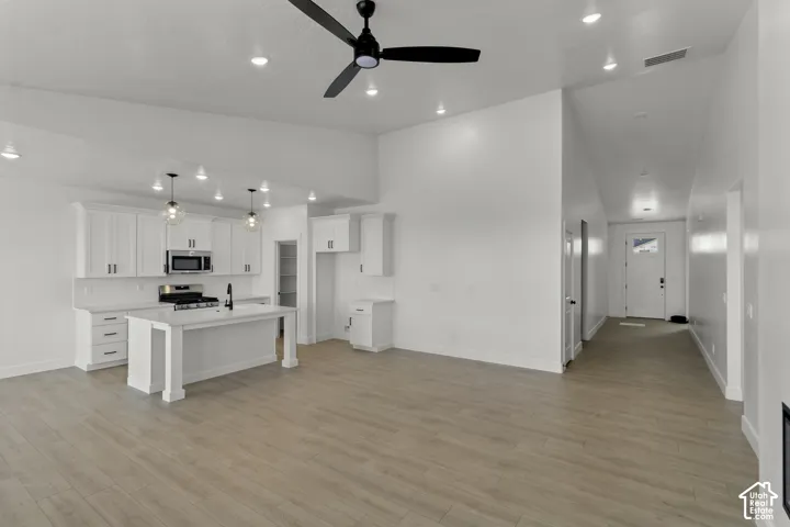 Open-concept living space featuring vaulted ceilings, wood-finish flooring, a kitchen island with seating, and stainless steel appliances