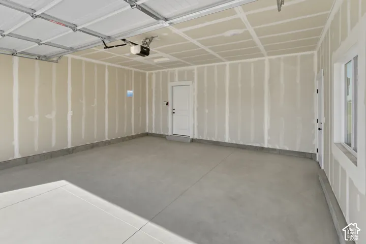 Concrete flooring, painted walls, overhead garage door, built-in window, and a white entry door