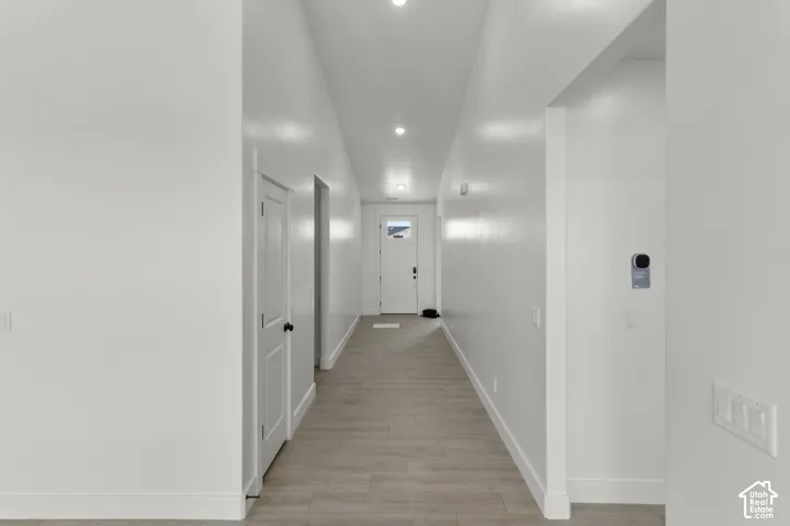 Hallway featuring recessed lighting, wood-finish flooring, white doors with black hardware, and a modern thermostat