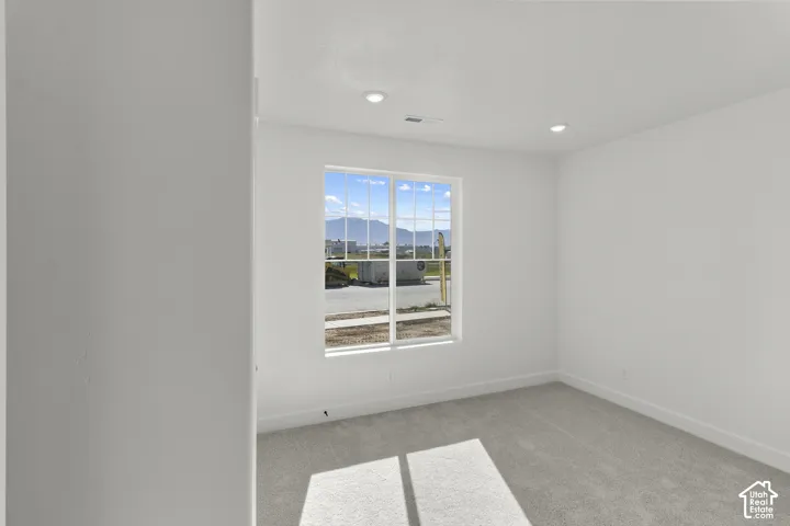 Recessed lighting illuminates this bright room featuring a window with grid patterns, light-toned carpeting, and crisp white walls