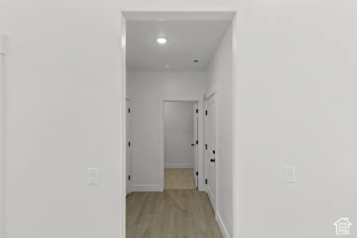 Recessed lighting illuminates the hallway with wood-finish flooring, white walls, white doors, and matte black hardware