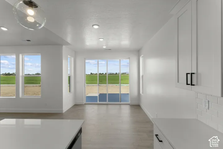 Recessed lighting, wood-finish flooring, white cabinetry with dark hardware, subway tile backsplash, and sliding glass doors
