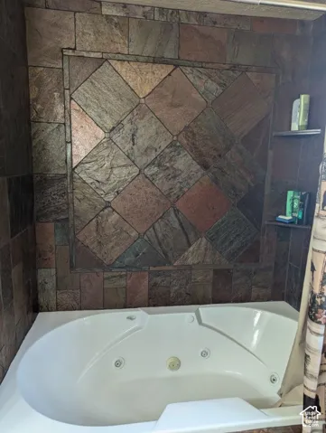 Jetted tub with integrated backrests, surrounded by natural slate stone wall tile with a diamond-pattern accent, and built-in wall shelving