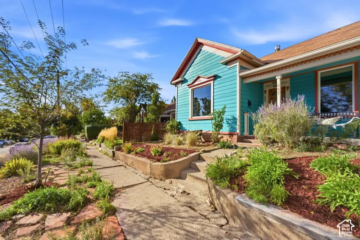 Vibrant turquoise exterior, red shingle roof,  stone paver accents, and planted garden beds