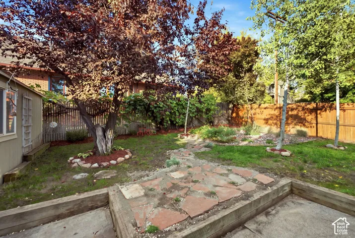Expansive backyard featuring a natural stone pathway, mature trees, wood fencing, and a built-in garden bed