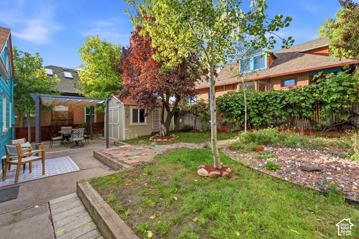 Spacious backyard featuring a concrete patio, shaded pergola, mature trees, and a storage shed