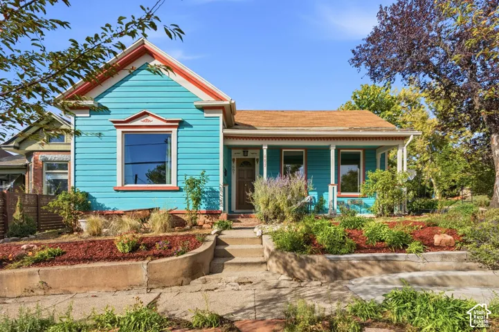 Vibrant turquoise exterior with contrasting trim, gabled roofline, covered front porch, and established landscaping with stepped retaining walls