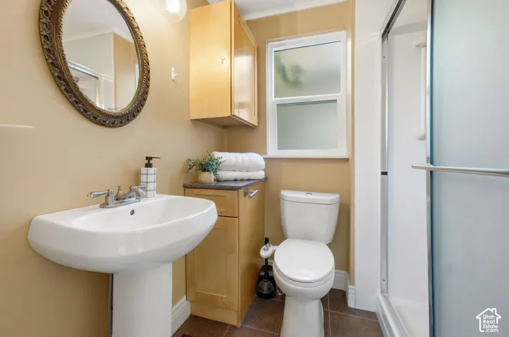 Pedestal sink, wood-finish cabinetry, frosted glass window, shower enclosure with sliding door, and tile flooring