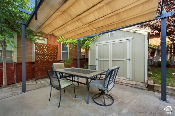 Concrete patio featuring a retractable pergola, privacy screen, and a storage shed