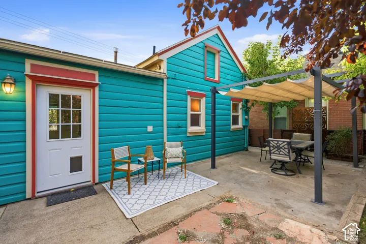 Turquoise siding exterior with red and white trim details, featuring a patio area with a retractable fabric pergola, and a glass-paned entry door with an exterior wall lantern