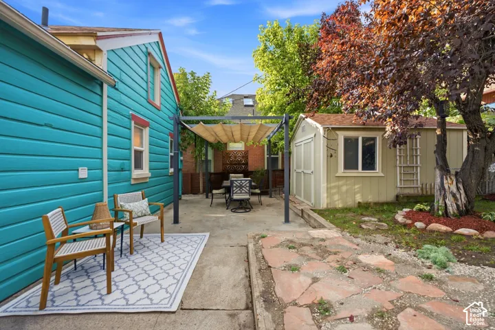 Paved patio area, pergola with retractable canopy, detached storage shed, flagstone pathway, and mature tree landscaping