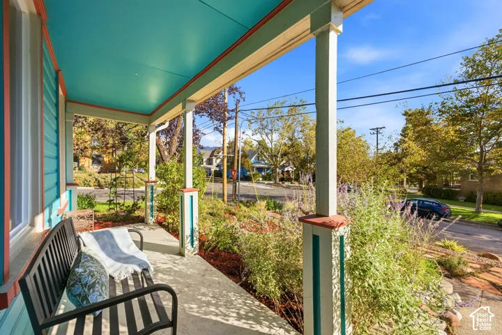 Covered front porch with painted teal ceiling and trim, concrete flooring, and established perimeter landscaping