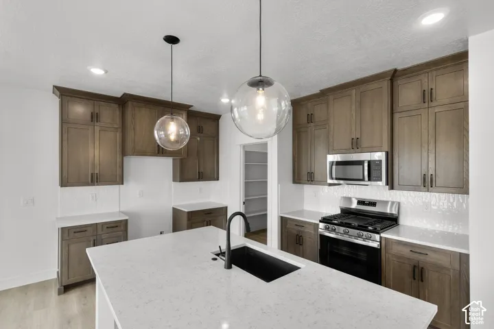 Kitchen featuring wood-finish cabinetry, white countertops, textured backsplash, stainless steel appliances, and two pendant lights