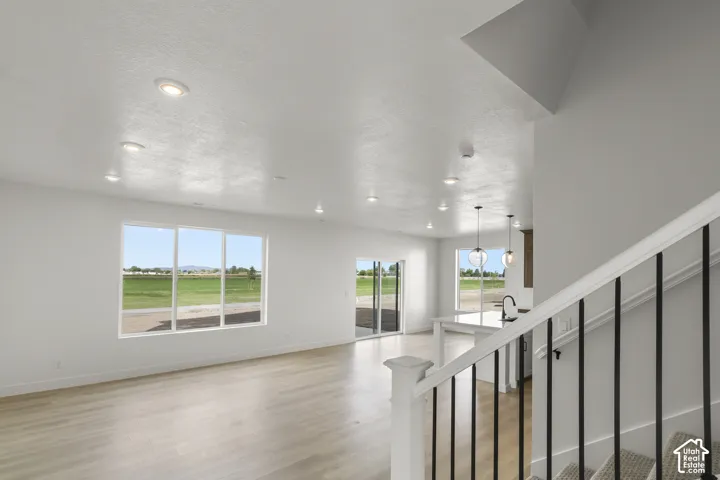 Recessed ceiling lighting, wood-finish flooring, large windows, sliding glass door, and a staircase with metal balusters