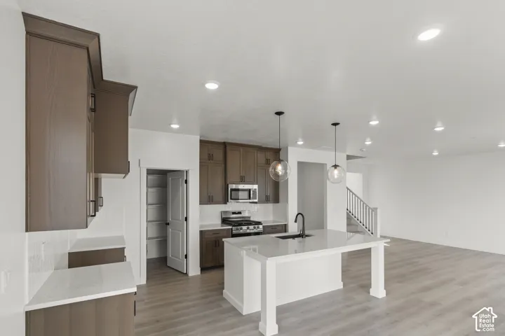 Kitchen featuring wood-finish cabinetry, white countertops, stainless steel appliances, and a central island with pendant lighting