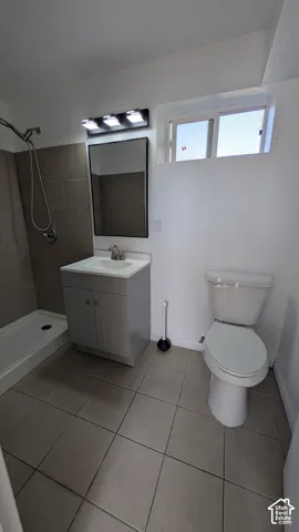 Tiled flooring, shower with tiled surround, vanity with integrated sink, rectangular mirror, and transom window