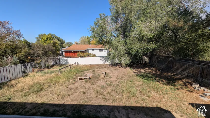 Expansive outdoor space featuring a sloped grade, established trees, a chain-link fence, and a white privacy fence
