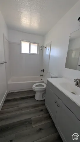 Wood-finish flooring, white bathtub and shower surround, light gray vanity with integrated sink, brushed nickel faucet, and a wall-mounted mirror
