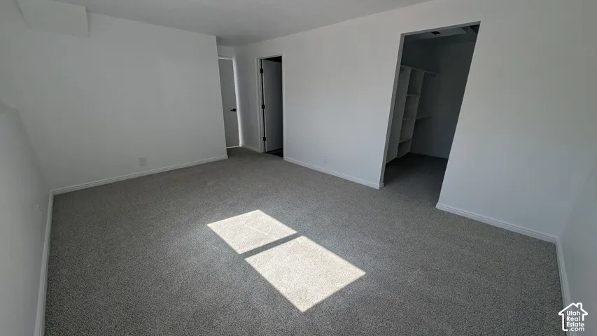 Gray carpeted flooring and white painted walls with an open closet featuring built-in shelving