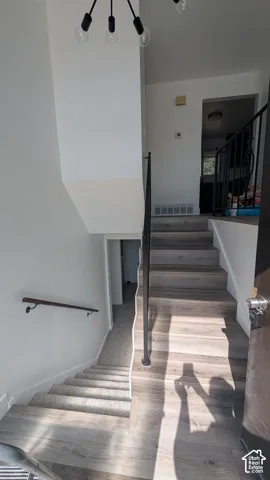 Multi-level entryway featuring wood-finish flooring, a modern chandelier, and a black metal handrail