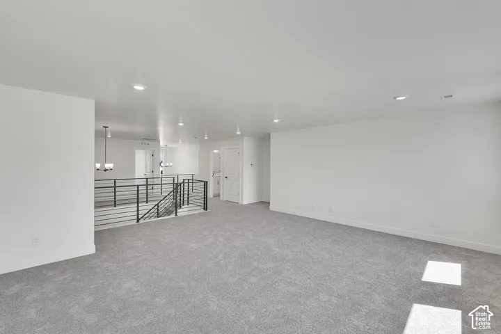 Spacious carpeted area with recessed lighting, white walls, and a modern horizontal bar railing
