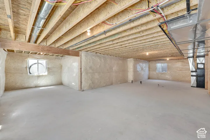 Unfinished basement space with exposed wood joists, concrete flooring, and insulated walls featuring two windows