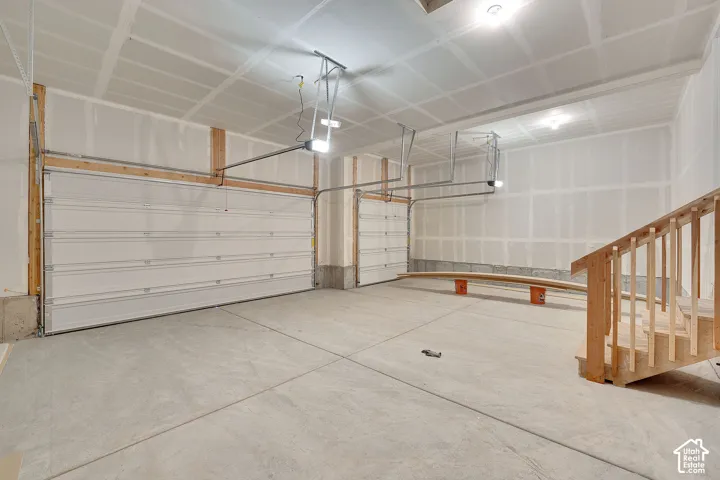 Two overhead garage doors, concrete flooring, unfinished drywall, and exposed wood framing