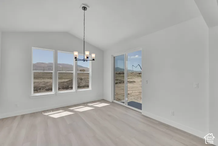 Vaulted ceiling with a contemporary chandelier, multiple large windows, light wood-finish flooring, and white walls