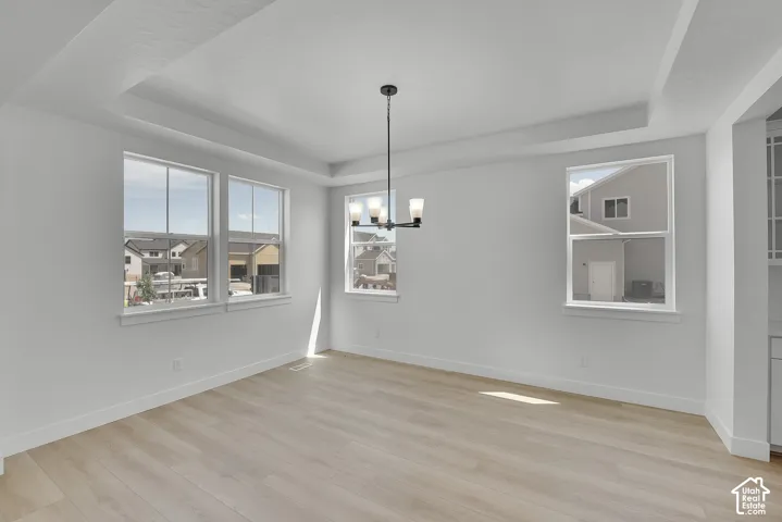 Recessed tray ceiling with an integrated chandelier, light wood-finish flooring, and multiple windows