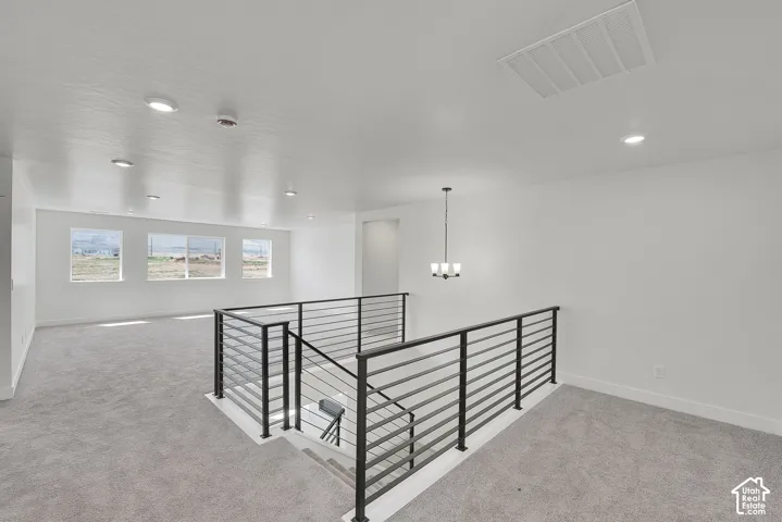 Open-concept loft area featuring a modern black horizontal bar railing, three large windows, recessed lighting, a contemporary chandelier, and light gray carpeting