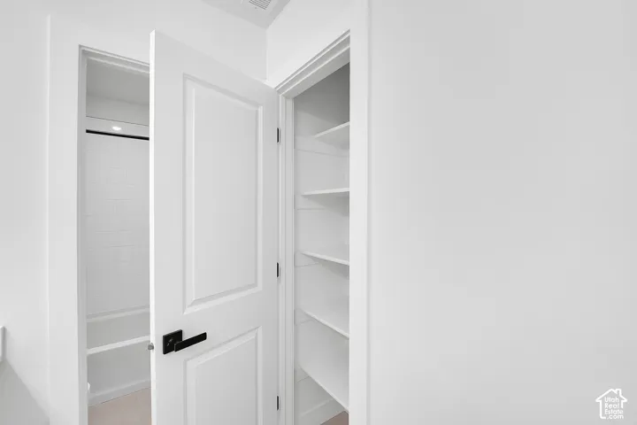 White paneled door with matte black hardware, built-in shelving, and a white tiled shower with tub